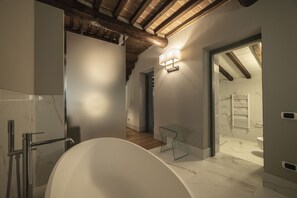 A modern bathroom with a freestanding bathtub, a glass shower enclosure, and a visible staircase leading to another room.