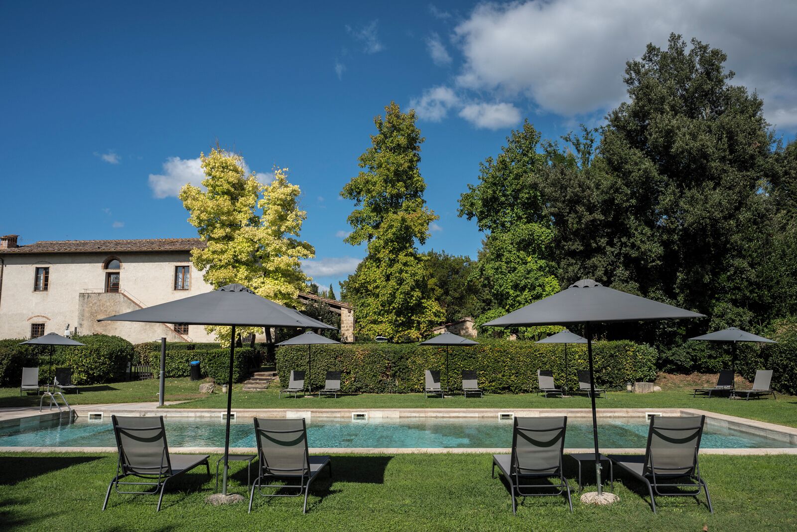 A poolside area with lounge chairs and umbrellas, a clear sky, and a building in the background.