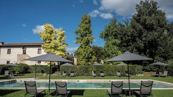 A poolside area with lounge chairs and umbrellas, a clear sky, and a building in the background.
