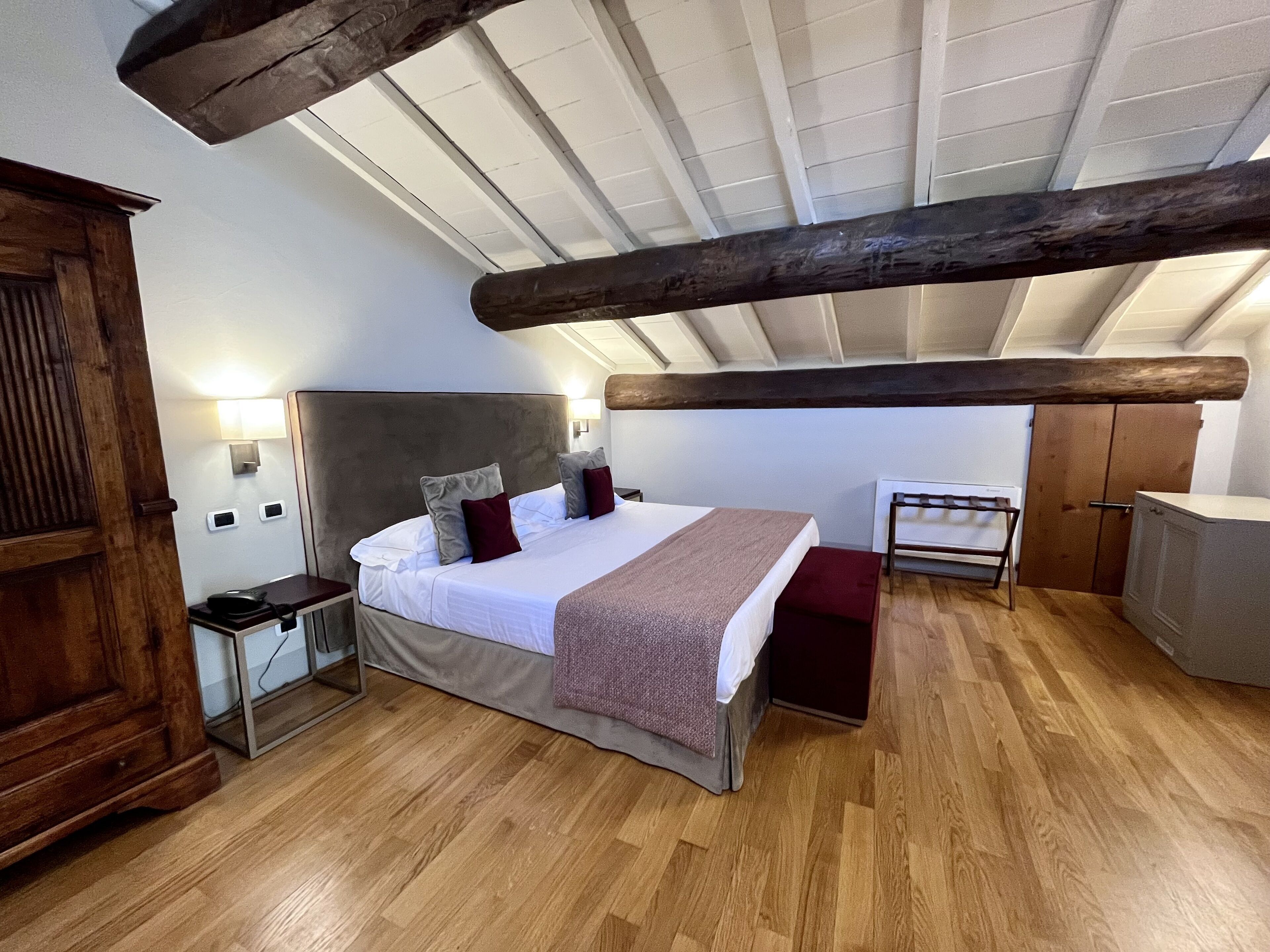 Ein Schlafzimmer mit einem großen Bett, Holzbalken, einem Nachttisch, einem Schreibtisch und einem Kleiderschrank.