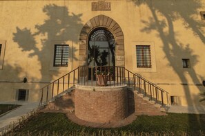 A building with a central arched entrance, a circular brick staircase, and a small balcony with a railing.