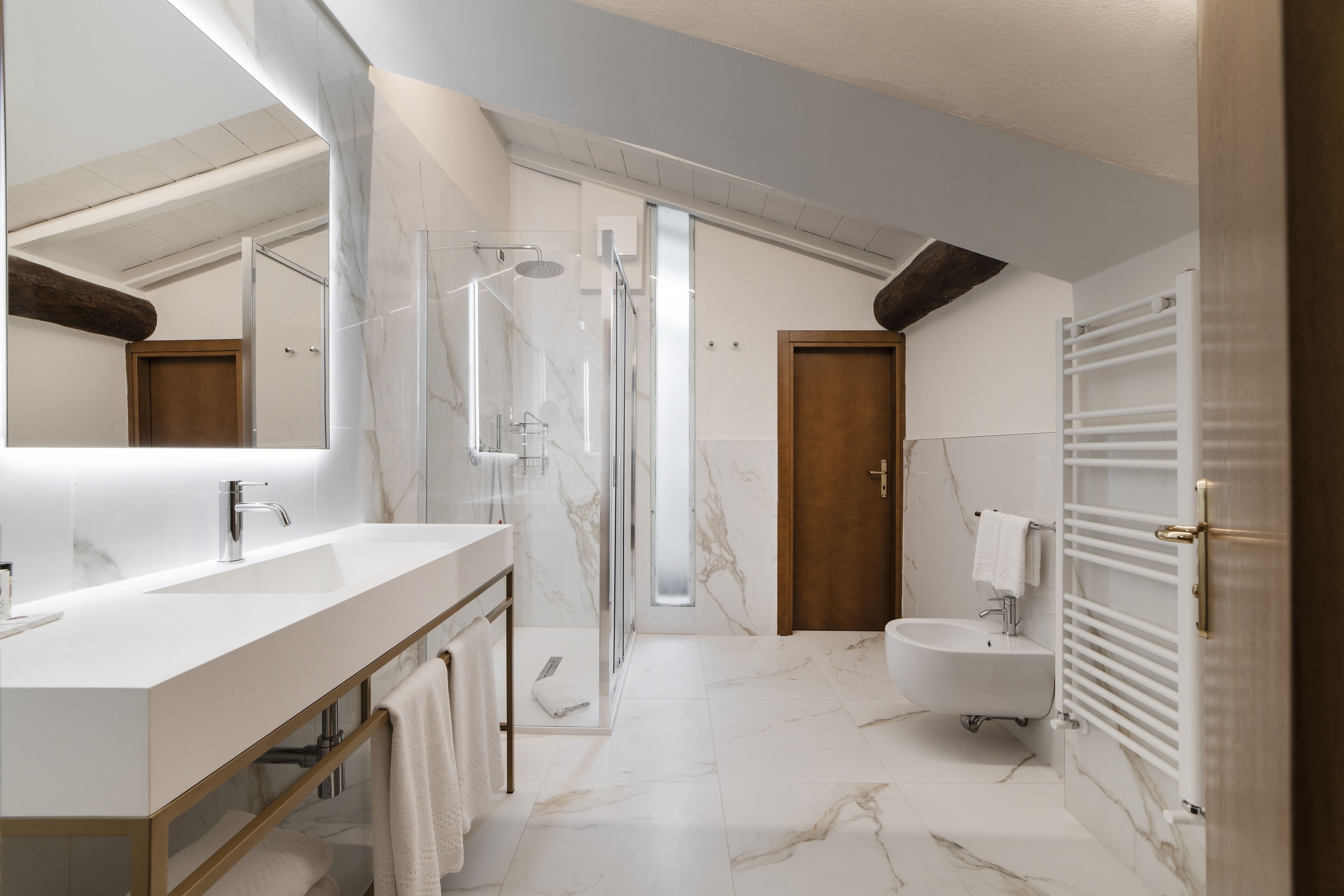 A modern bathroom with a large mirror, a shower, a bidet, and a vanity with a sink and towel rack.