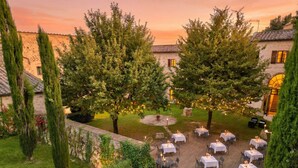 An outdoor dining area with tables and chairs, surrounded by trees and a stone wall. - Relais Della Rovere (Colle di Val d'Elsa)