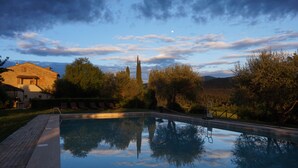 A swimming pool with a clear reflection, surrounded by trees and a building with a sloped roof. - Relais Castel Bigozzi (Monteriggioni)