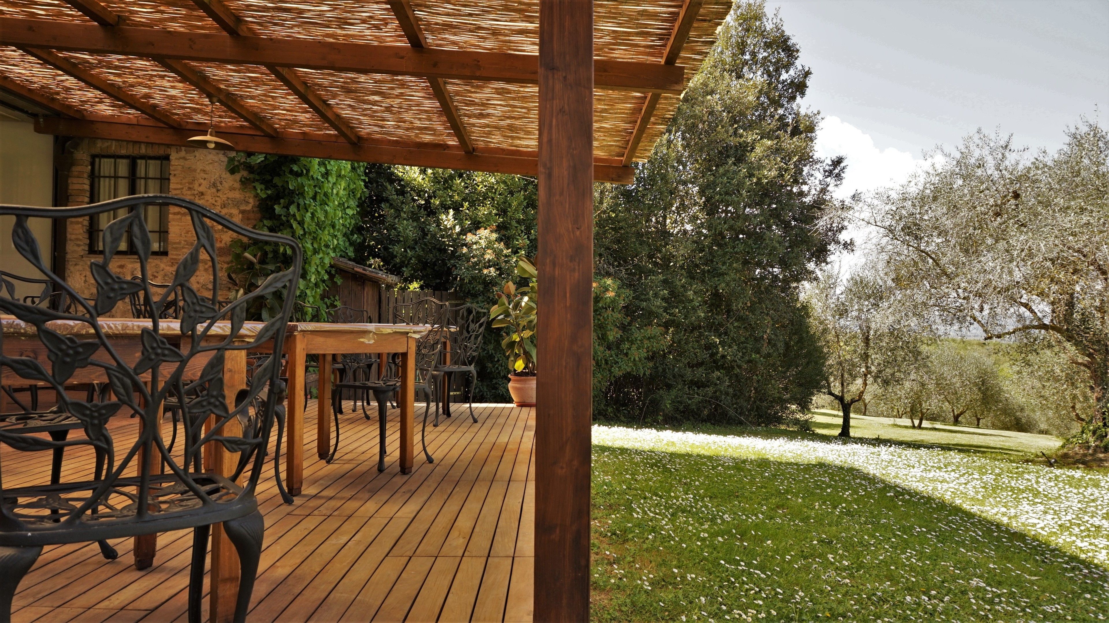 A wooden deck with outdoor furniture, a pergola, and a garden with trees and white flowers.