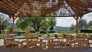 A wooden gazebo with a thatched roof overlooking a landscaped garden with trees and a view of hills. - Relais Castel Bigozzi (Monteriggioni)