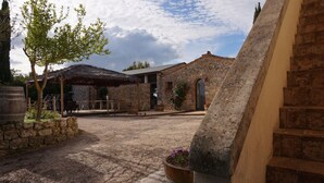 A courtyard with stone buildings, a thatched-roof structure, and potted plants. - Relais Castel Bigozzi (Monteriggioni)