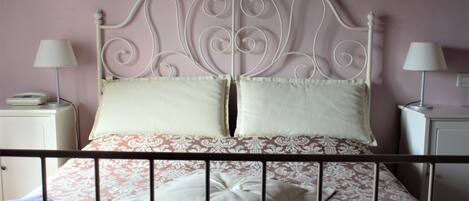 A neatly made bed with a decorative headboard, two bedside lamps, and a stack of folded towels on the side.