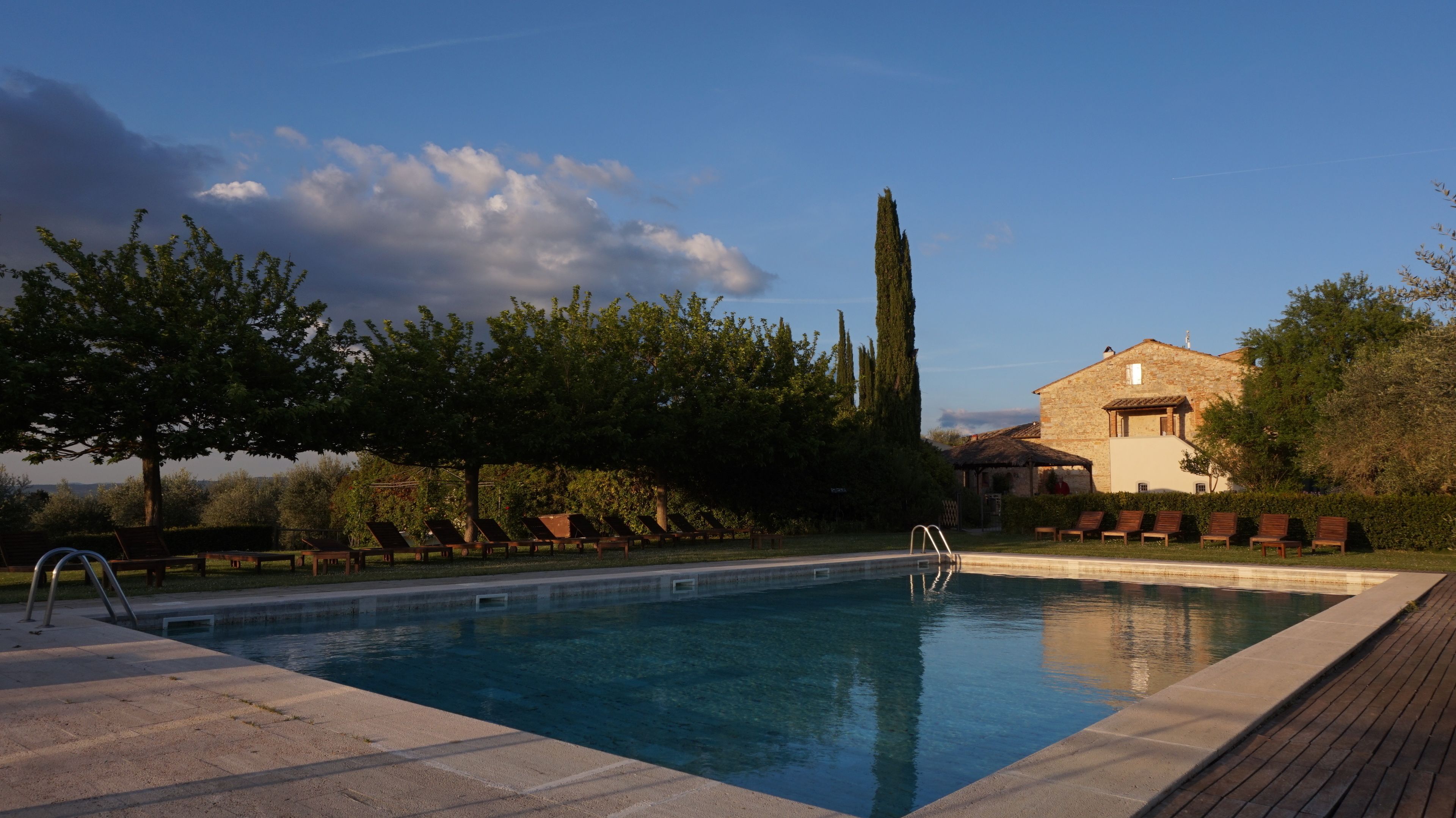 A swimming pool with lounge chairs, a stone building, and a tall tree.