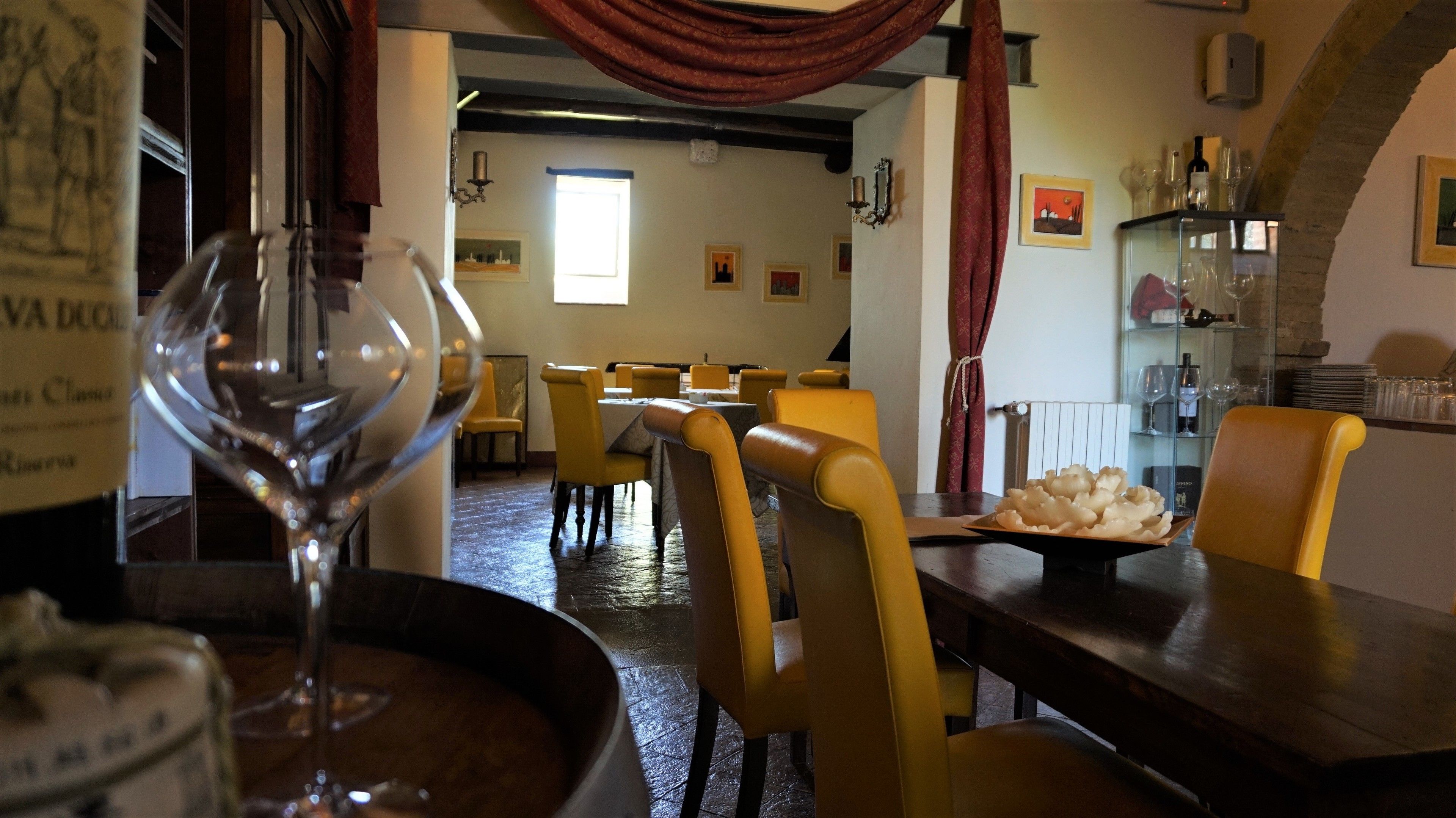Ein Restaurantinneres mit gelben Stühlen, einem Tisch mit einem Teller Essen und einem Weinglas.
