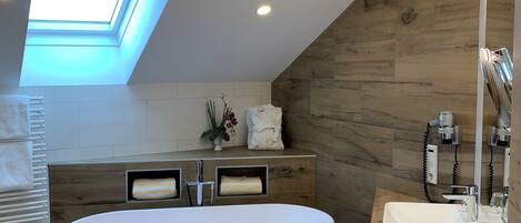 A modern bathroom with a skylight, a freestanding bathtub, a vanity with a sink, and wooden wall panels.