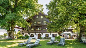 A traditional chalet with a balcony, surrounded by lush greenery and outdoor seating. - Romantik Hotel die Gersberg Alm mit Panorama über Salzburg und Outdoorpool ab Mai (Salzburg)