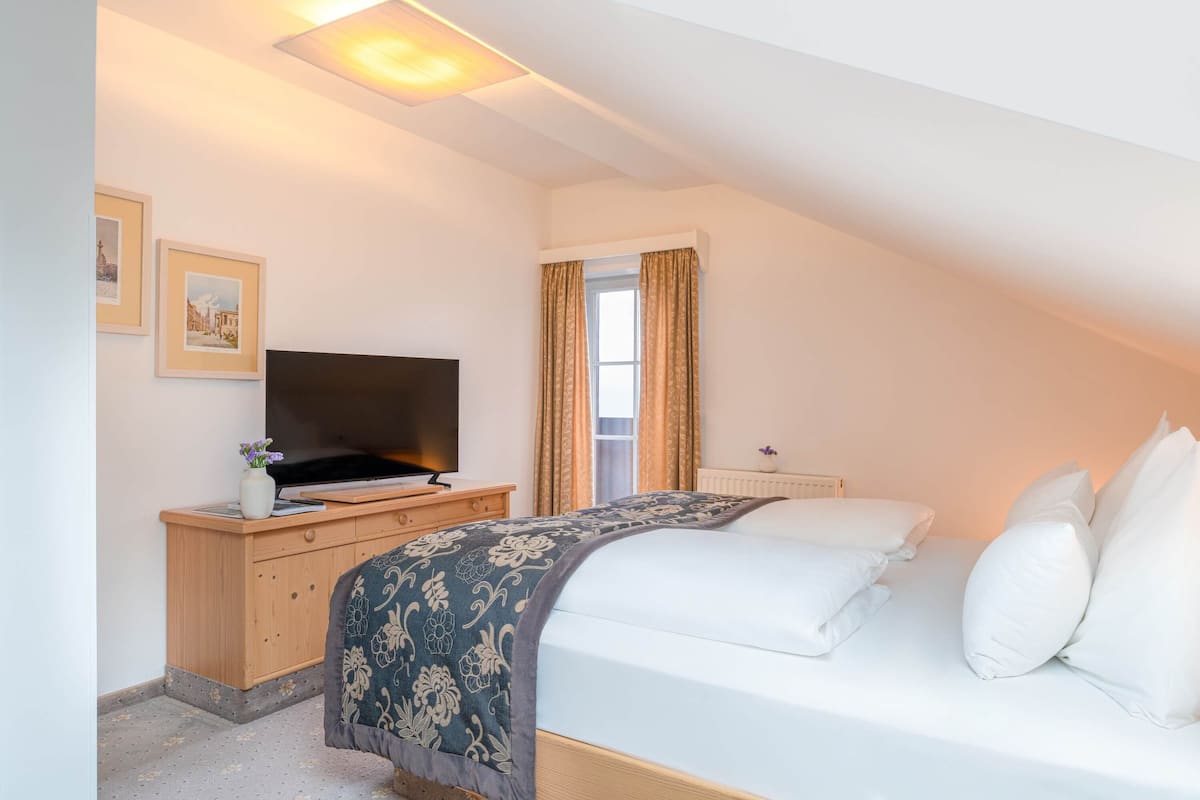 A bedroom with a bed, a TV on a wooden dresser, and a window with curtains.