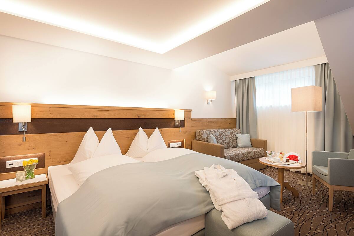 A hotel room with a large bed, a sofa, a small table, and a lamp.