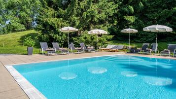 A swimming pool with lounge chairs and umbrellas, surrounded by trees.