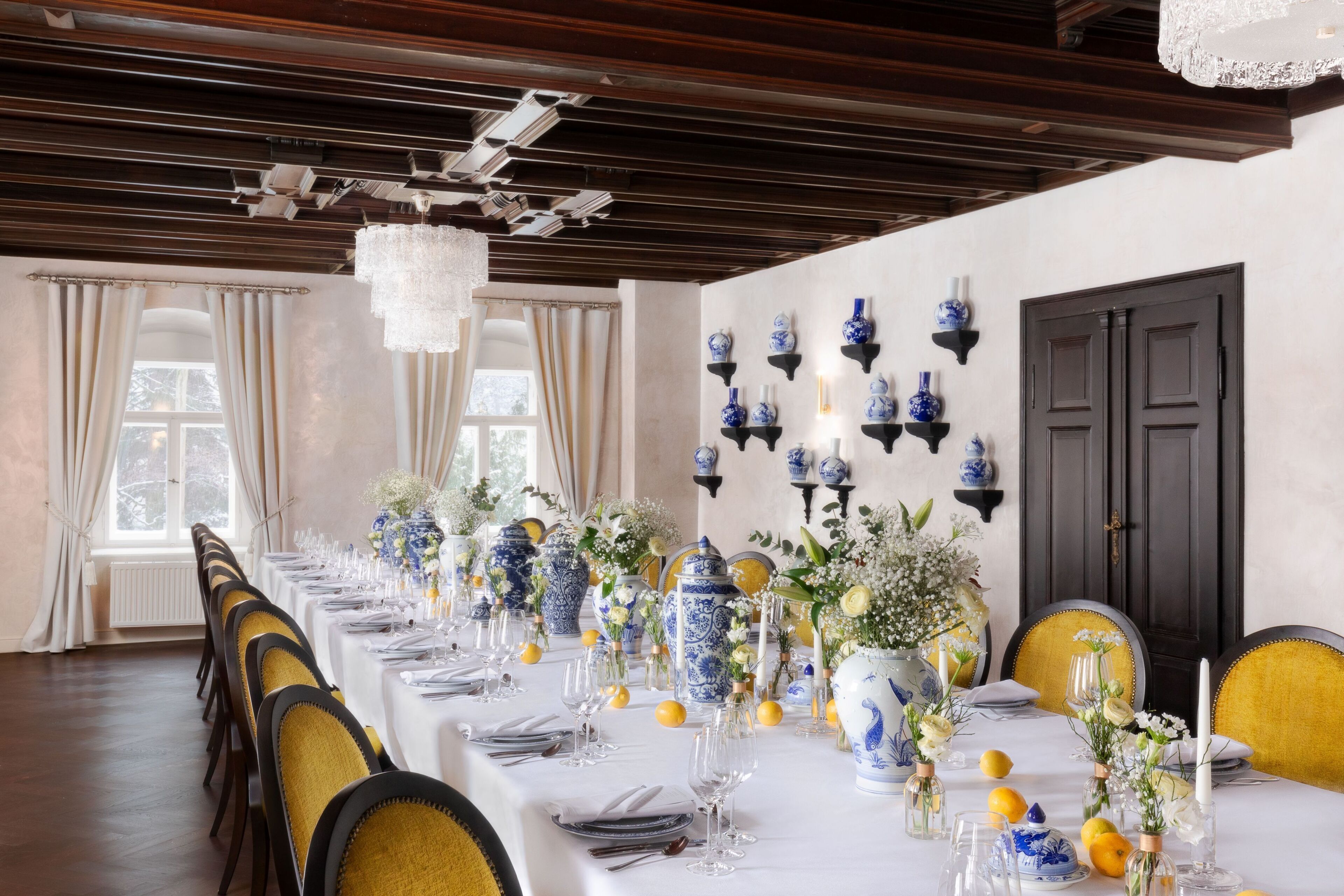 A long dining table set with chairs, blue and white vases, and floral arrangements.