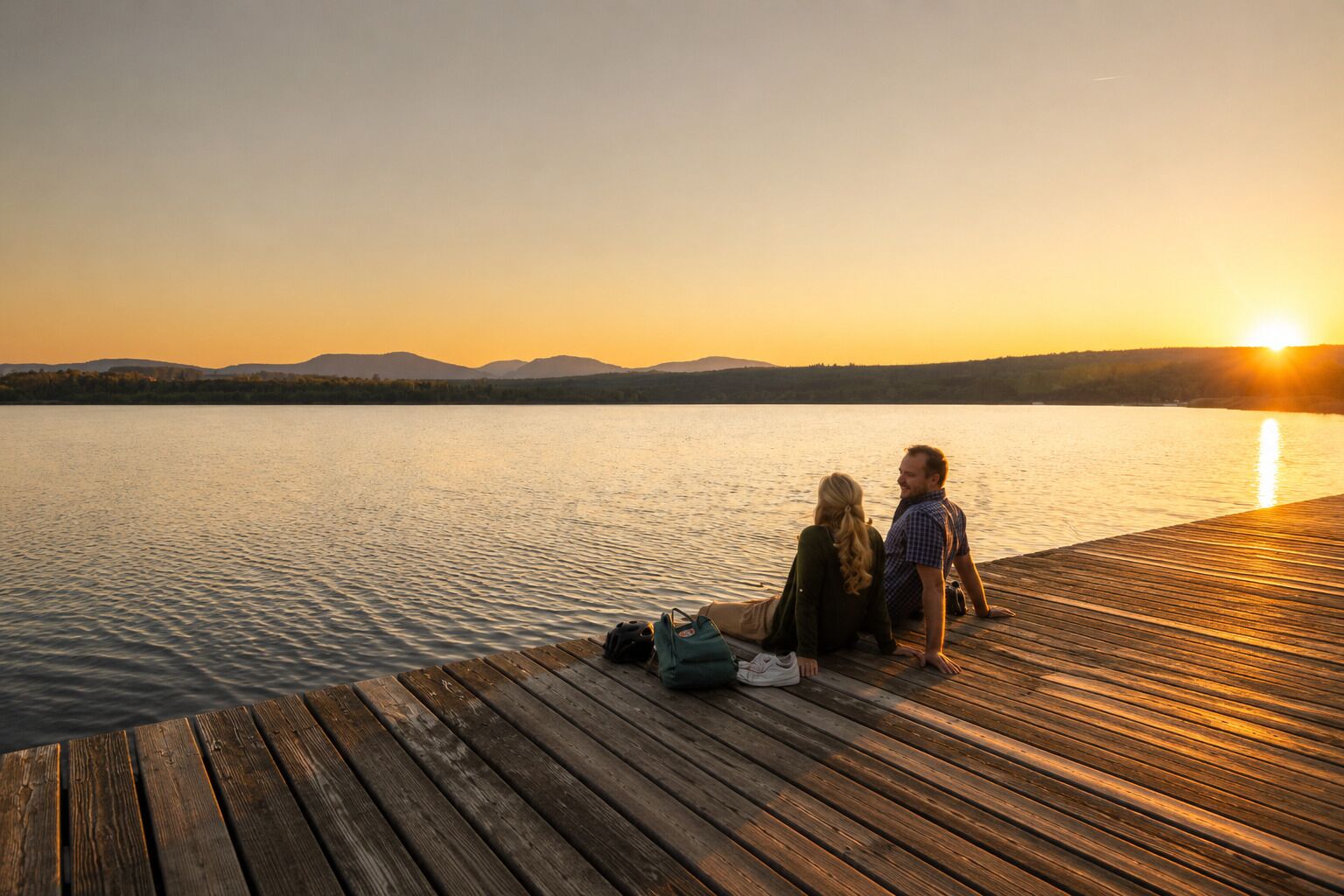 A wooden dock extending into calm water with a sunset in the background.