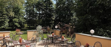 Un patio al aire libre con mesas y sillas, rodeado de follaje y árboles.