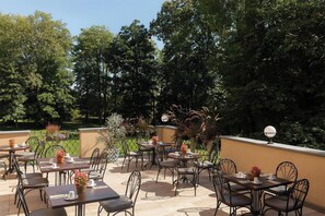 An outdoor patio with tables and chairs, surrounded by greenery and trees. - Schlosshotel Althörnitz (Bertsdorf-Hoernitz)