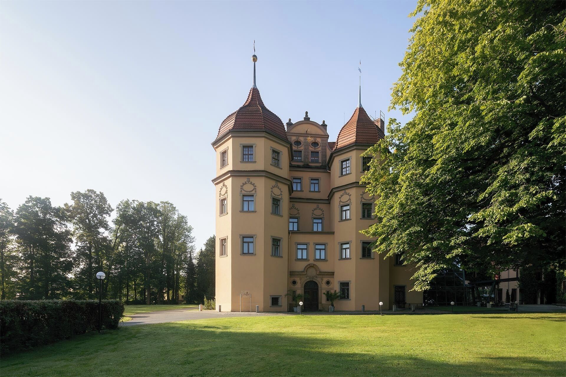 A large, multi-story building with a central tower and multiple smaller towers, surrounded by a well-maintained lawn and trees.