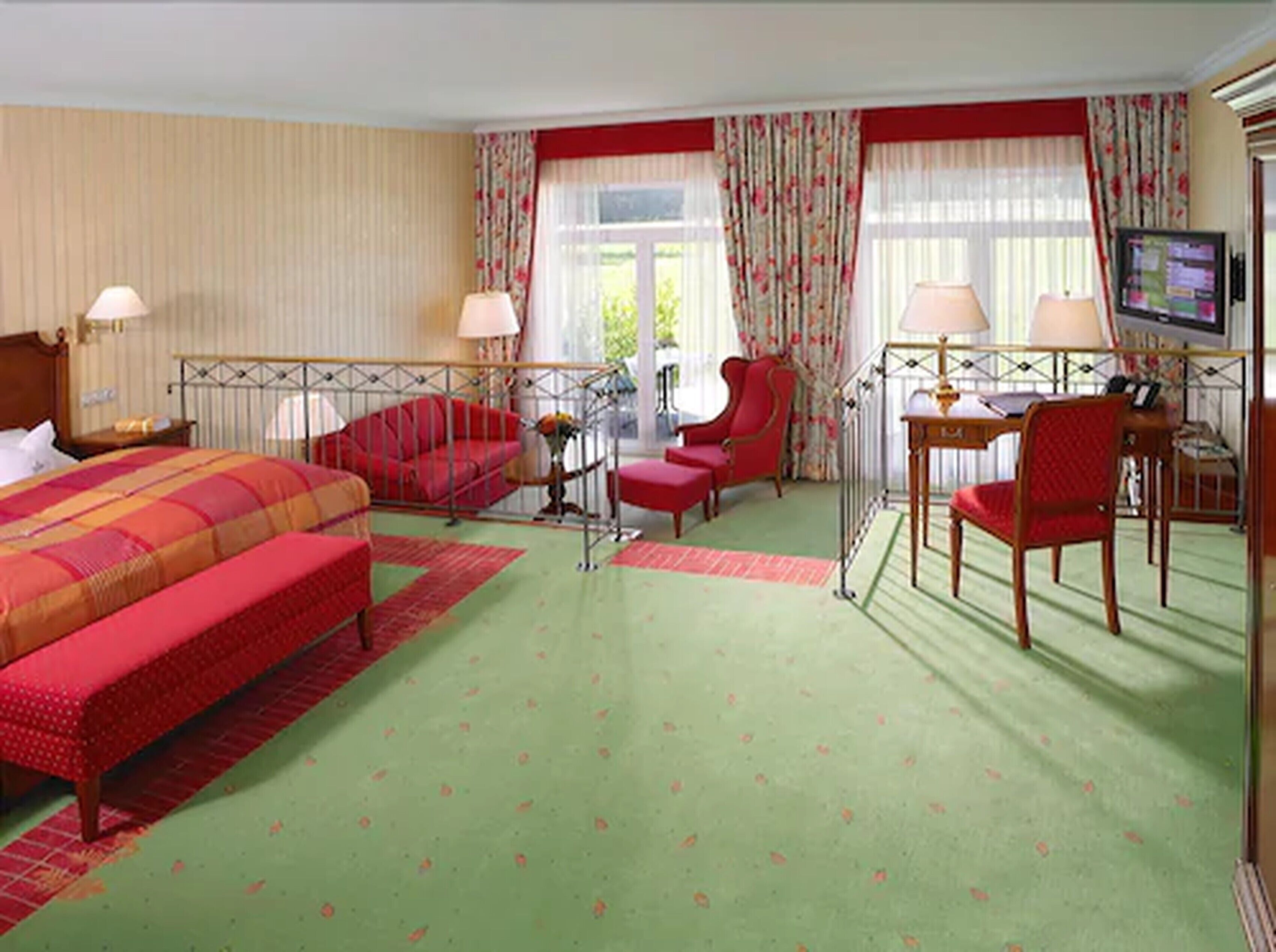 Une chambre d’hôtel avec un lit, un canapé rouge, un fauteuil rouge, un bureau avec une chaise et un téléviseur.