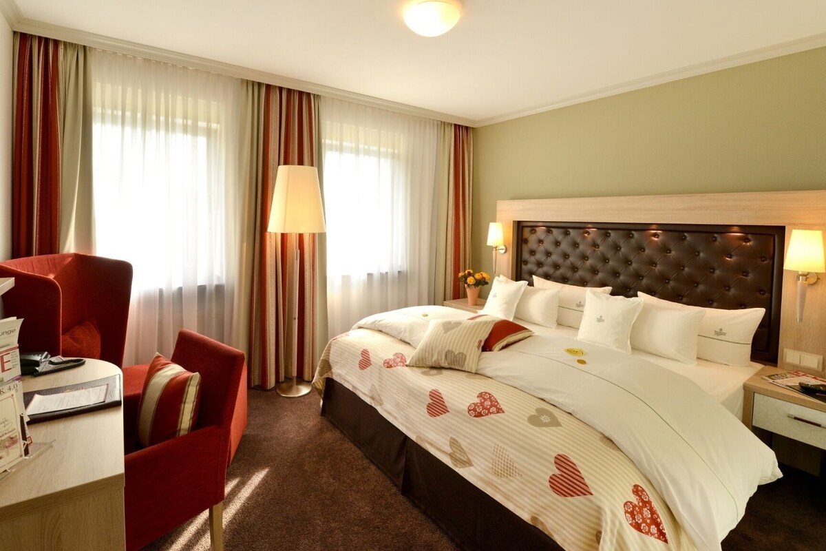 Une chambre d’hôtel avec un grand lit, un bureau avec une chaise, une lampe et un tableau au mur.