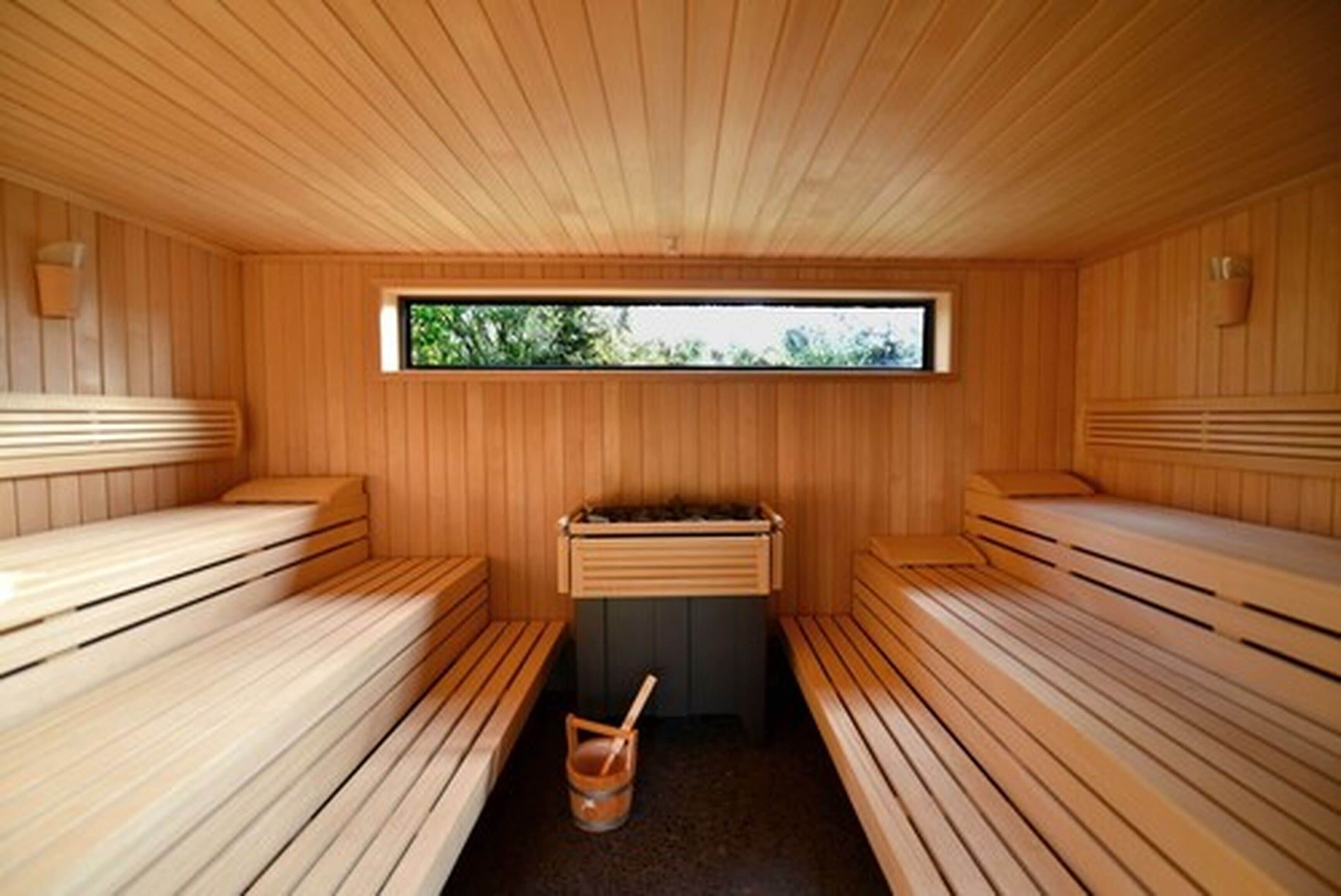 A sauna with wooden benches, a window, and a bucket.