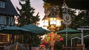 An outdoor patio with checkered tablecloths, wooden chairs, and a table lamp with flowers. - Lohmann's Romantik Hotel Gravenberg (Langenfeld)