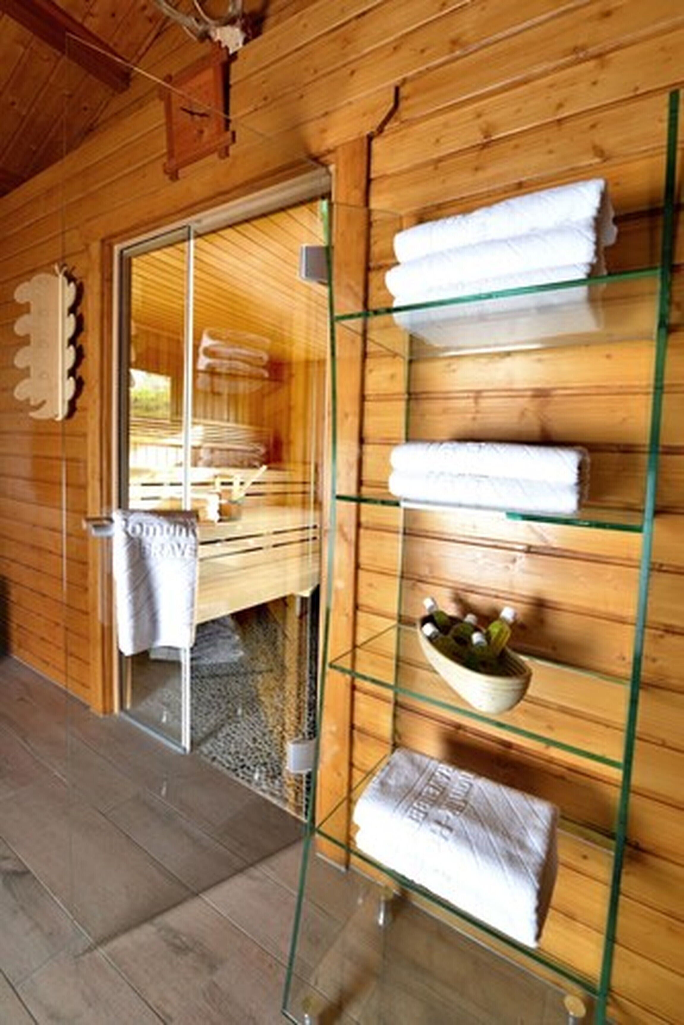 Ein Holzblockhaus-Interieur mit Glastür zum Saunabereich, Handtücherregalen und einer Flaschenschale.