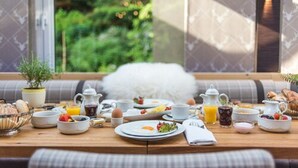 A breakfast table set with various dishes and drinks, a potted plant, and a view of greenery through a window. - Lohmann's Romantik Hotel Gravenberg (Langenfeld)