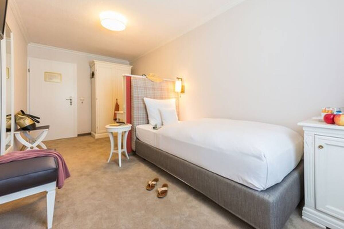 Una habitación de hotel con una cama, una mesita de noche pequeña, una silla, un armario y una puerta.