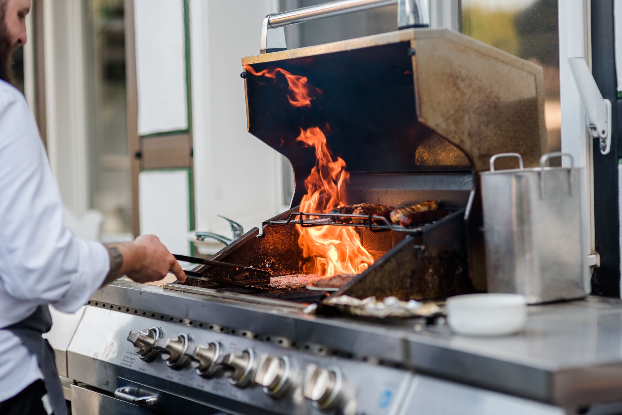 Un chef cuisinier prépare des aliments sur un grill professionnel, et les flammes sont bien visibles.