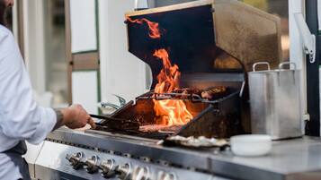 Un chef cuisinier prépare des aliments sur un grill professionnel, et les flammes sont bien visibles.