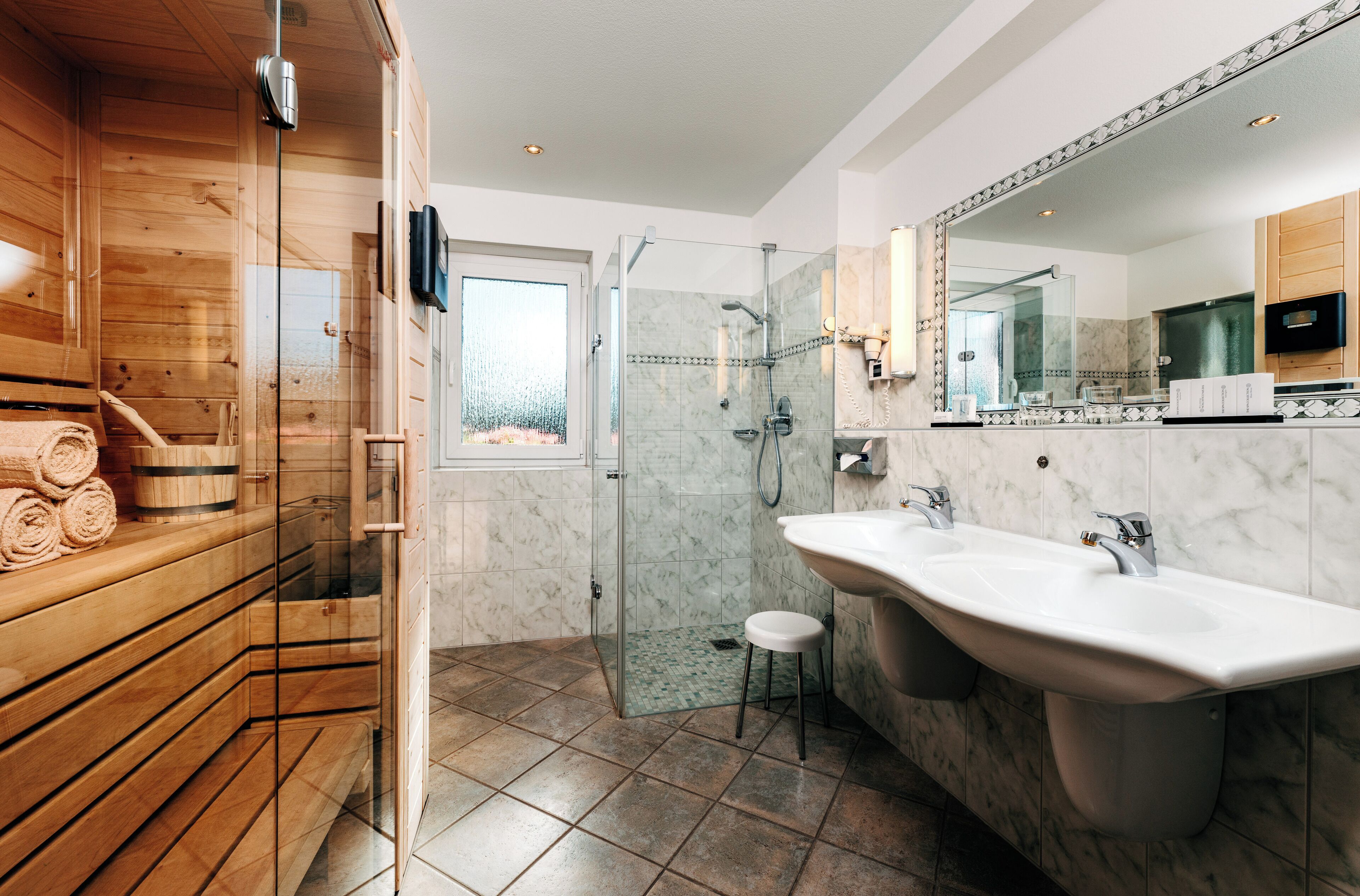 A modern bathroom with a wooden sauna, a glass-enclosed shower, and a large mirror.