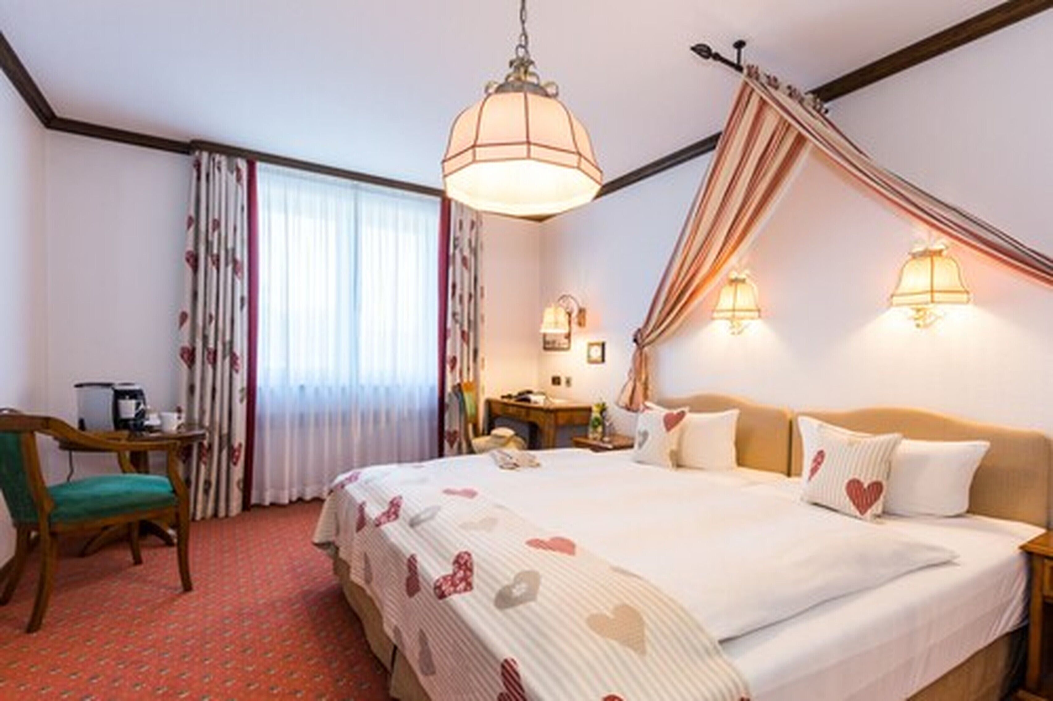 A hotel room with a large bed, a desk, a chair, and a window with curtains.
