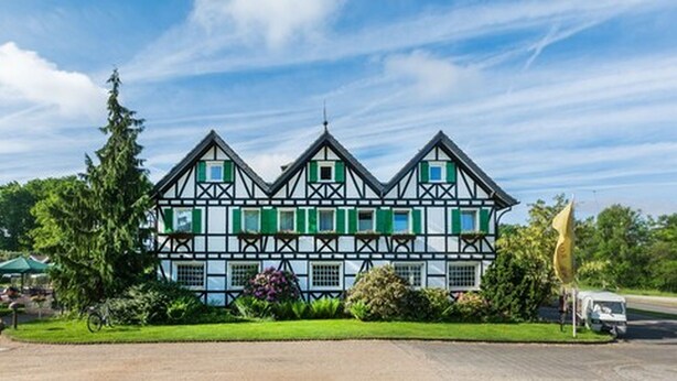 A large, traditional half-timbered building with multiple gabled roofs, surrounded by well-maintained gardens and a clear sky. - Lohmann's Romantik Hotel Gravenberg (Langenfeld)