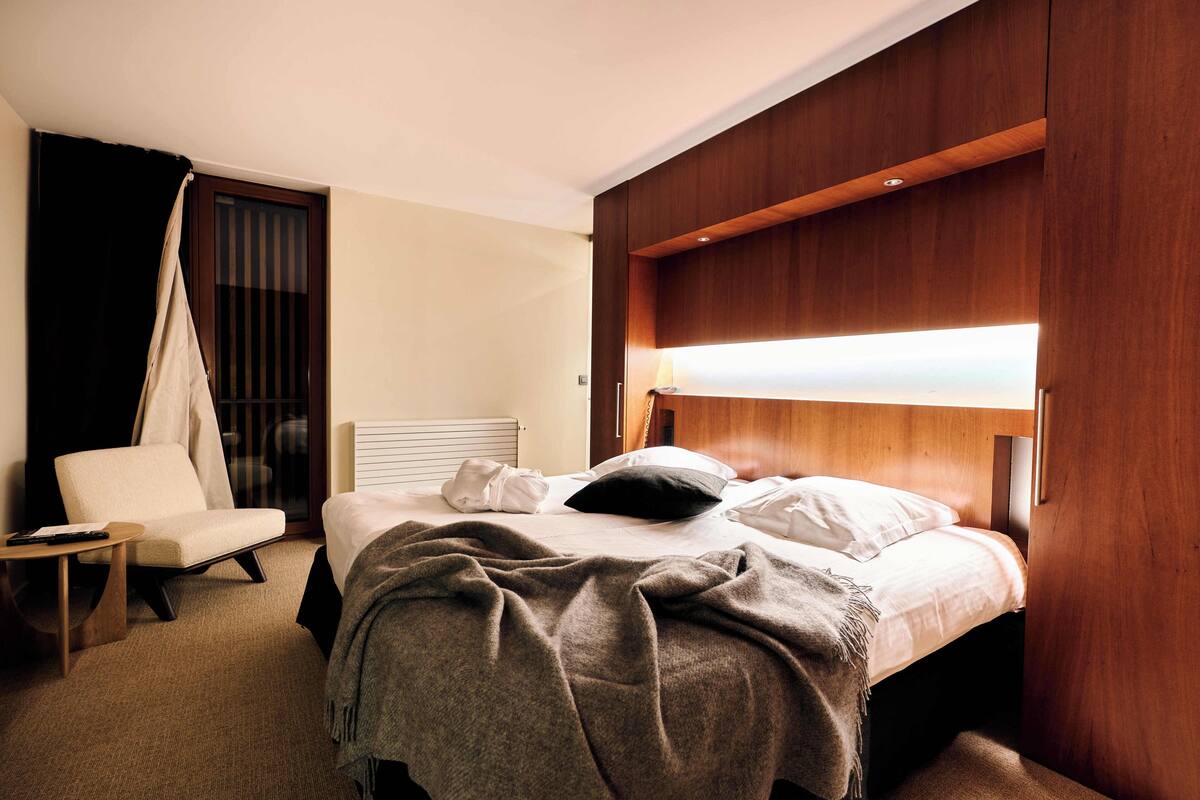Una habitación de hotel con cama, una silla, una mesita de noche y un dosel.