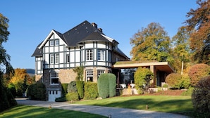 A large, two-story house with a curved section, surrounded by well-maintained gardens and a cobblestone driveway. - Romantik Hotel Le Val d'Amblève (Stavelot)
