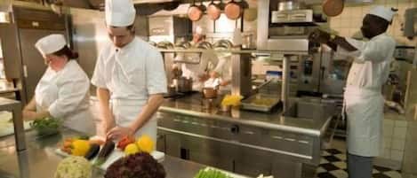 A professional kitchen with chefs preparing food, stainless steel appliances, and a checkered floor.