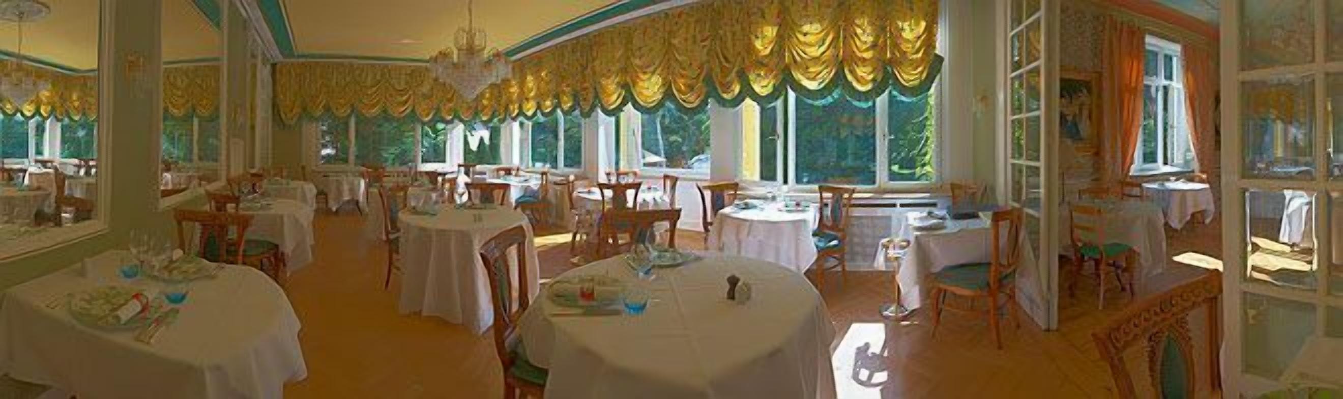 A dining area with round tables, chairs, and a large window with curtains.