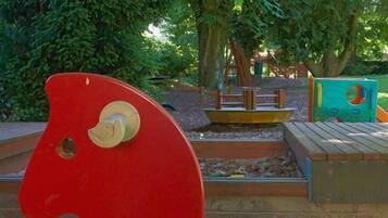 Una estructura de juego con forma de caballo rojo en un parque, con árboles y un banco de madera al fondo.