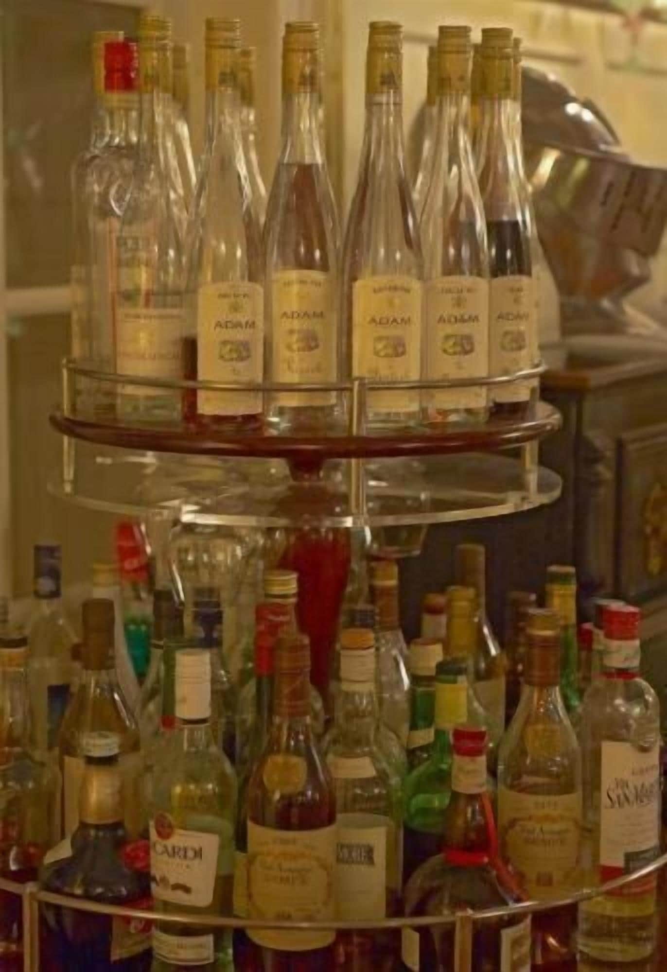 Een gelaagde presentatie van verschillende sterke drank flessen, waaronder merken als Adam en Cardo, geplaatst op een metalen standaard.