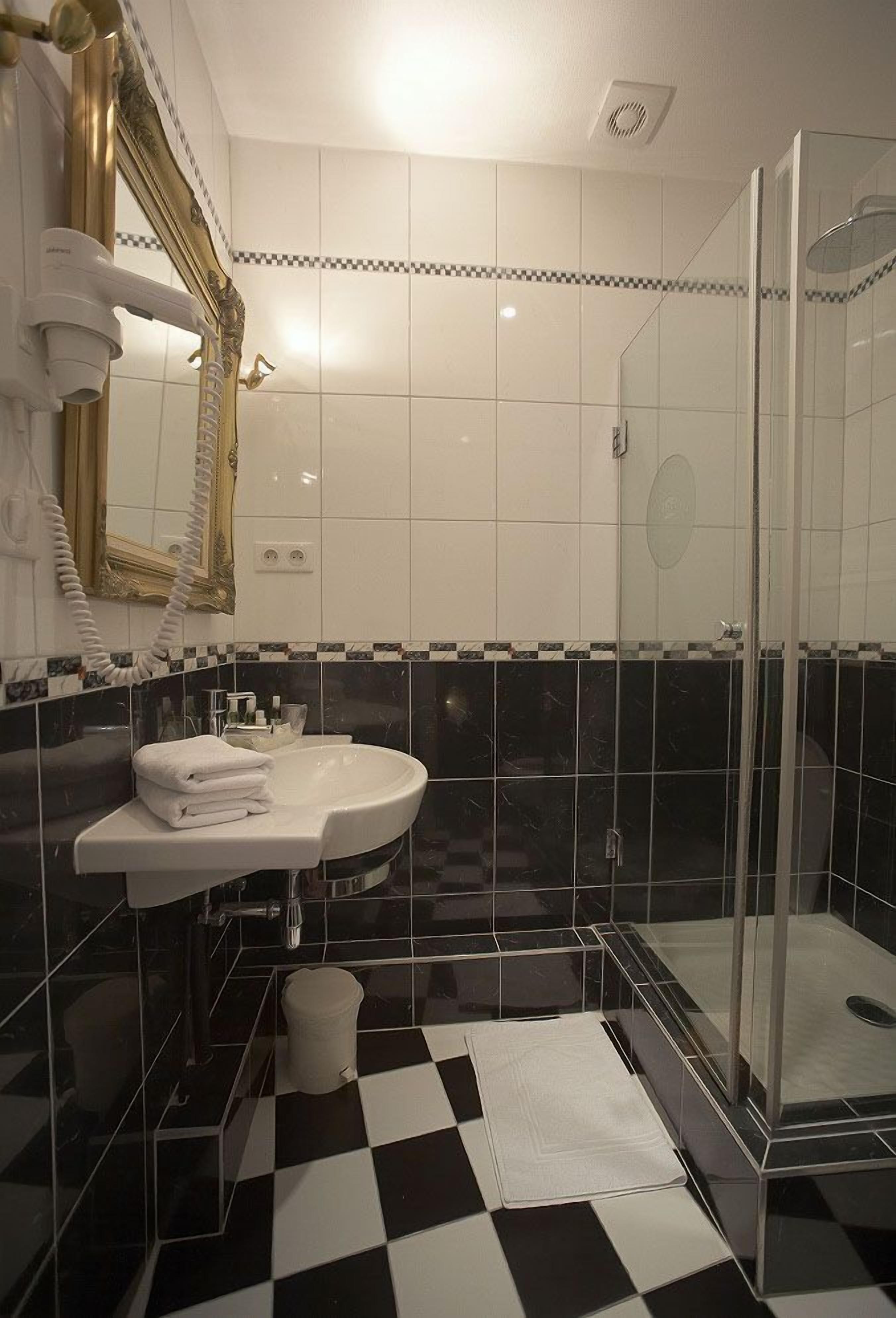 A bathroom with a white sink, a mirror, a glass shower enclosure, and checkered floor tiles.