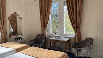 A hotel room with two beds, a large mirror, a table with a lamp, and two chairs.