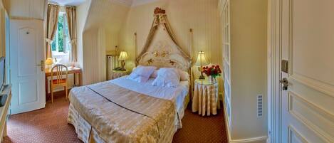 A bedroom with a four-poster bed, a desk with a chair, a television, and a window with curtains.