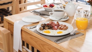 Une table de petit-déjeuner avec des assiettes remplies de nourriture, une théière, des tasses et un verre de jus d’orange.