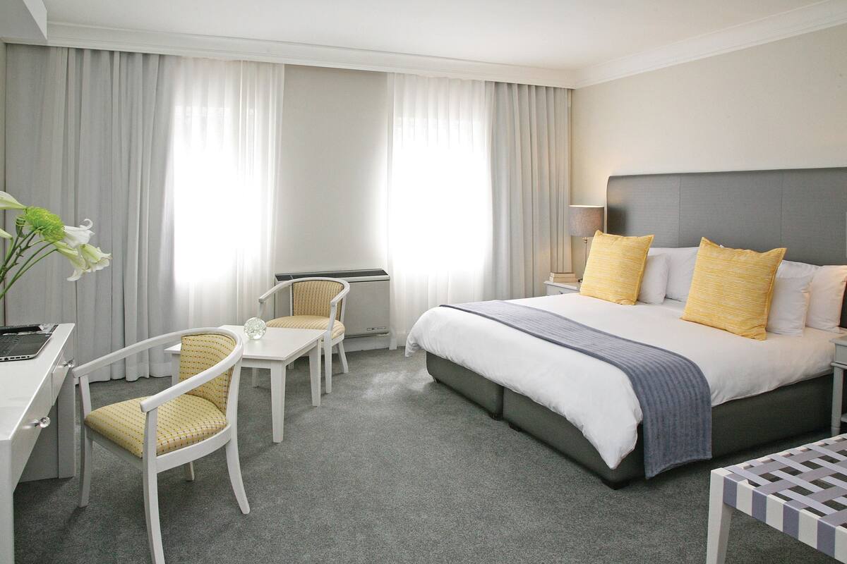 Ein Hotelzimmer mit einem Bett, zwei Stühlen, einem Schreibtisch und einer Lampe.