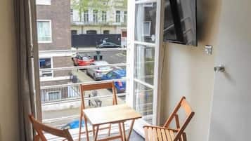 A room with a table and two chairs, a television on the wall, and a view of a street outside.