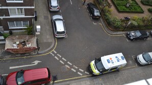 A street view with parked cars, a police vehicle, and a dumpster.