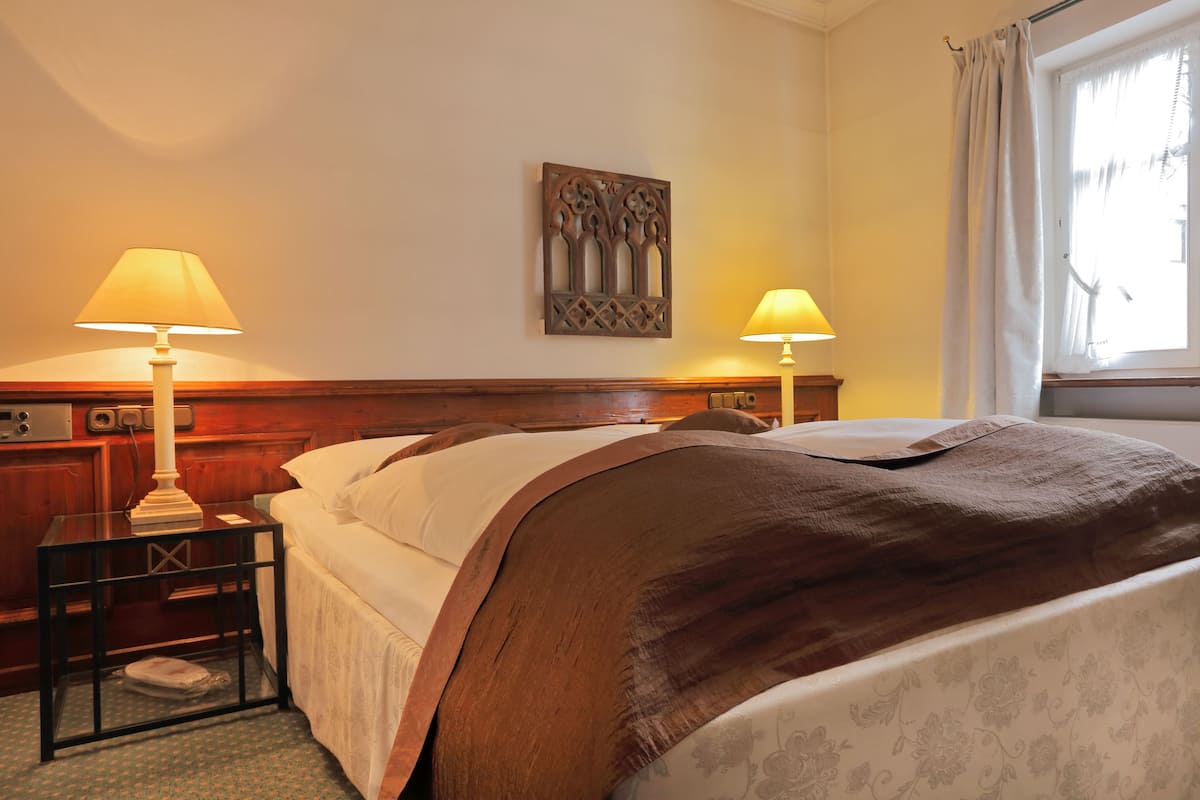 A hotel room with a bed, two bedside tables with lamps, a decorative wall piece, and a window with curtains.